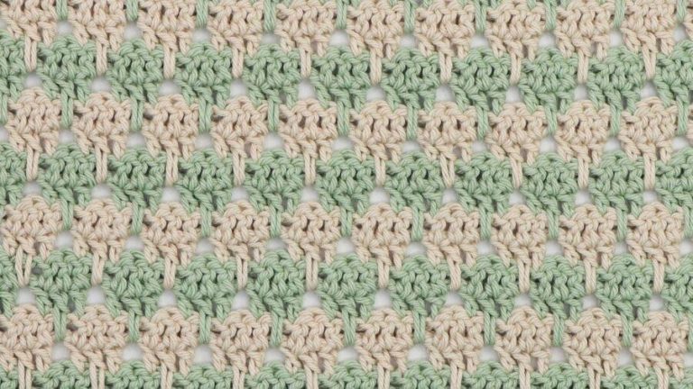 Close-up of crochet larksfoot stitch pattern in alternating rows of sage green and cream yarn. The stitch design features vertical elongated loops resembling bird footprints, creating a textured, repeating geometric pattern.