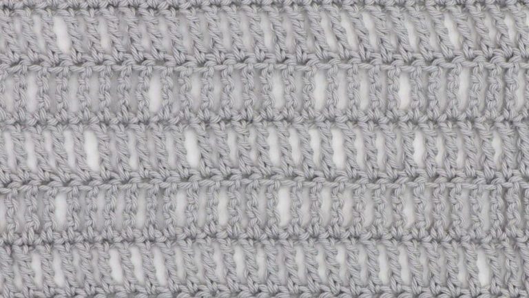 Close-up of a crochet fabric made using the triple treble stitch, showing tall, elongated stitches in light gray yarn with visible vertical gaps for an airy, lacy texture.