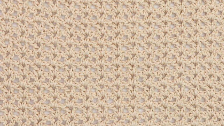 Close-up of a beige crochet swatch using the V-stitch, showing a lacy and open texture with a repeating V-shaped pattern.