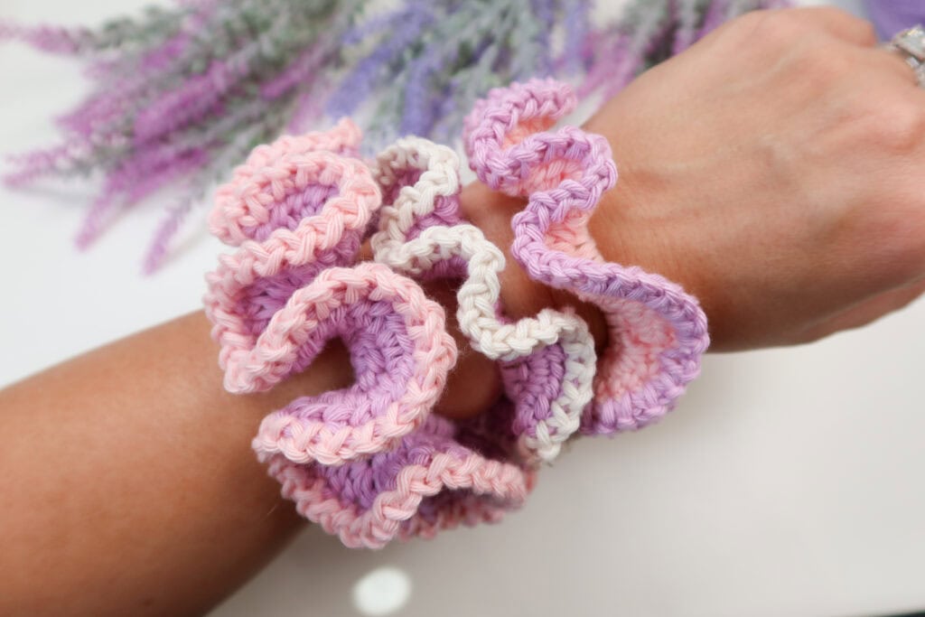 Three crochet scrunchies on a woman's wrist. 