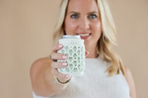 female holding a crochet can cosy in cream and green yarn. Held int