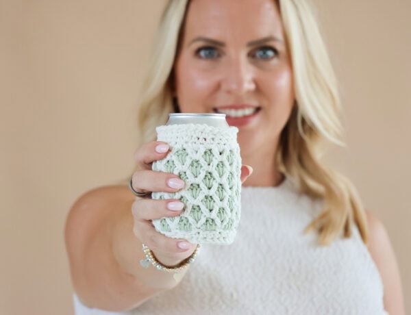 female holding a crochet can cosy in cream and green yarn. Held int