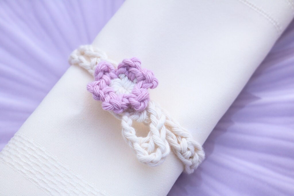 crrochet napkin holder wrapped around a white napkin lay on a purple plate.